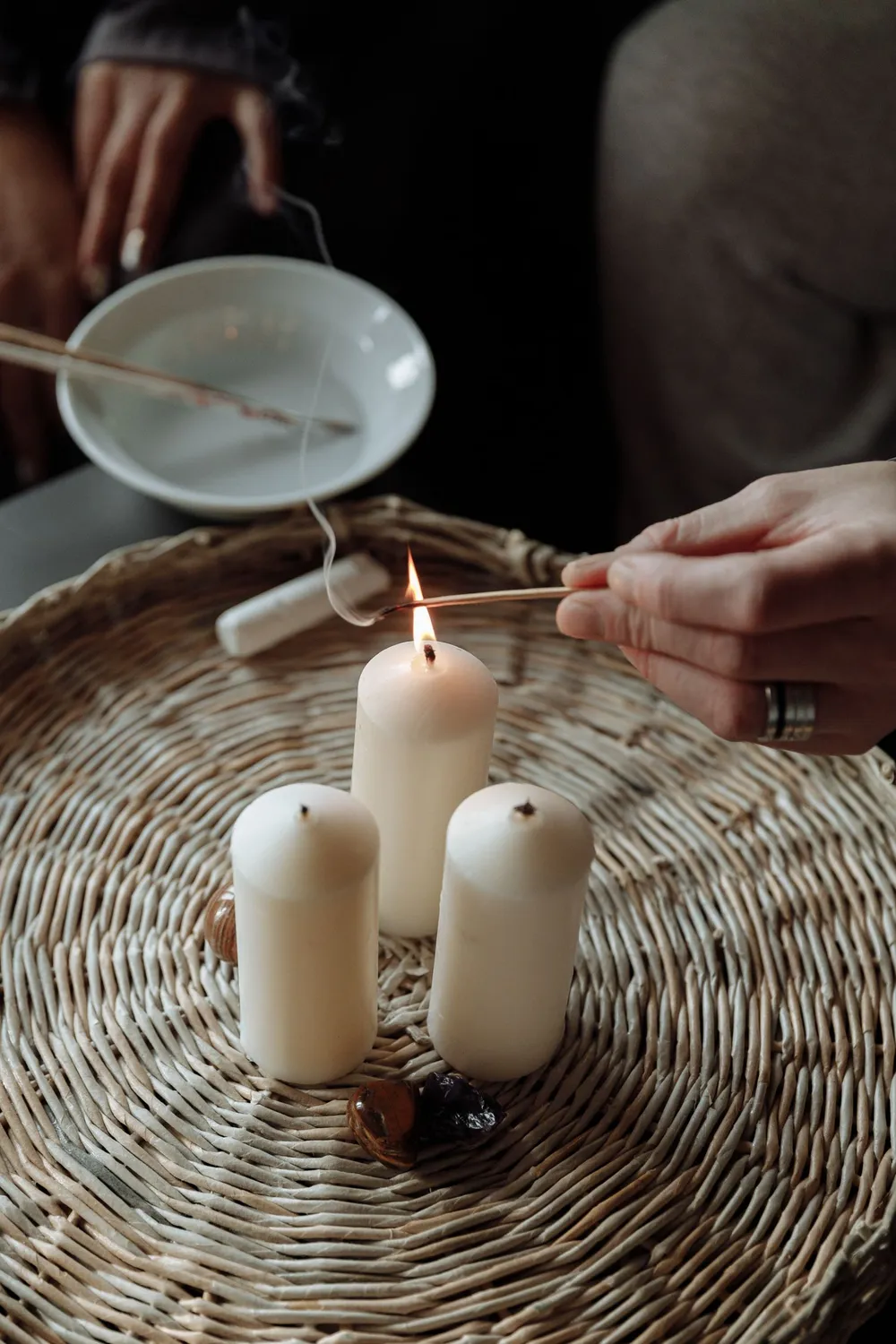 Mão acendendo velas brancas sobre um cesto de palha, para o ritual de abertura de caminhos