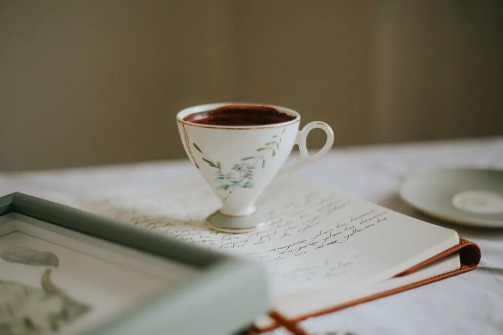 Xícara de chá sobre um caderno aberto com anotações manuscritas, em ambiente tranquilo e com luz suave