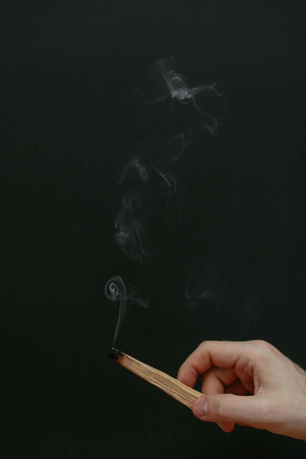 Mão acendendo um bastão de palo santo, com fumaça subindo